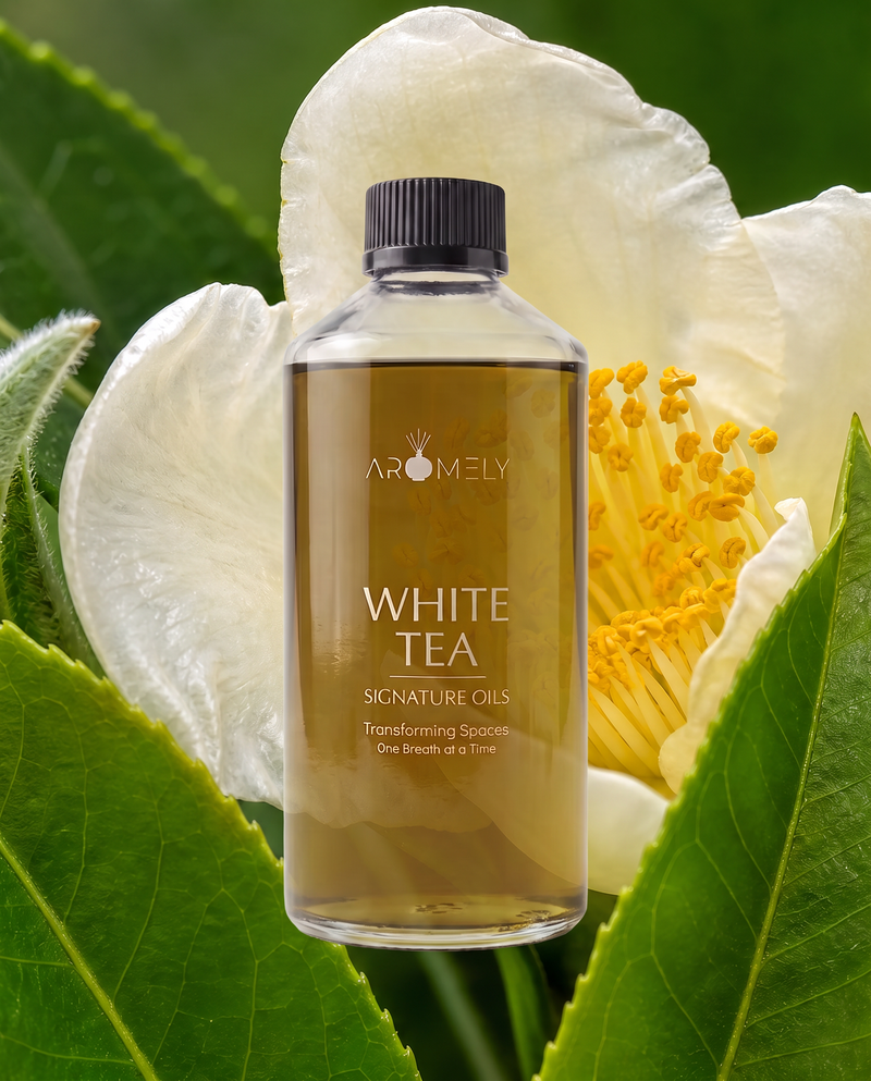 A clear bottle of Aromely White Tea Signature Oils with a black cap, set against a background of white camellia flowers and green leaves.