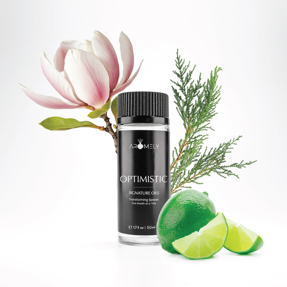 Aromely Optimistic diffuser oil in a sleek black 50ml bottle, surrounded by fresh limes, magnolia flowers, and cypress leaves. A bright, uplifting citrus scent for home or office aromatherapy.